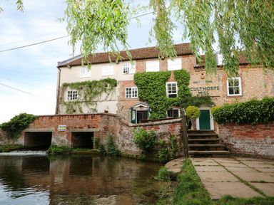 An old brick building with ivy climbing on the walls by a river with a stone bridge and steps leading up to a green door at Culthorpe Mill
