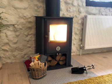 A wood burning stove with fire inside a room with stone walls and wooden floor at Far Barn in Fakenham