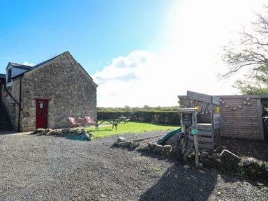 An outdoor area with a stone building, picnic table, and playhouse at Cattle Shed near Narberth