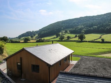A wooden house with a slate roof near green fields and hills at Meadow View in Meifod Powys