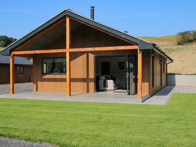 A brown wooden house with a covered patio and lawn at Meadow View in Meifod Powys