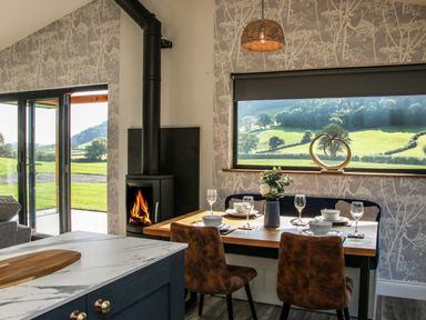 Dining area with table set for four near a window and wood burning stove at Meadow View in Meifod Powys