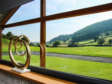 A decorative sculpture on a windowsill with a view of green fields and hills at Meadow View in Meifod Powys