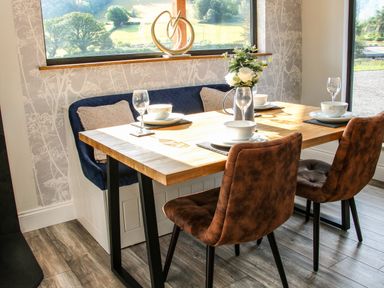 A dining area with a wooden table set for four with bowls wine glasses chairs and bench seating at Meadow View in Meifod Powys
