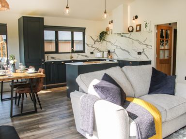 A kitchen and dining area with dark cabinets and marble backsplash and a gray sofa with cushions and blankets at Meadow View in Meifod Powys