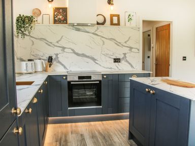 A kitchen with blue cabinets and marble countertops and backsplash with wooden flooring at Meadow View in Meifod Powys