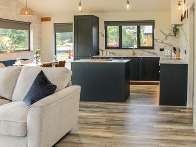 An open plan living room and kitchen with a light gray sofa a dining table dark cabinets and marble countertops at Meadow View in Meifod Powys