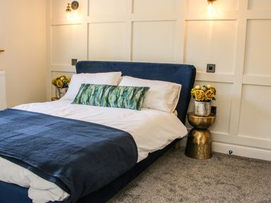 A bedroom with a blue bed framed by white paneled walls and bedside tables with flowers at Meadow View in Meifod Powys