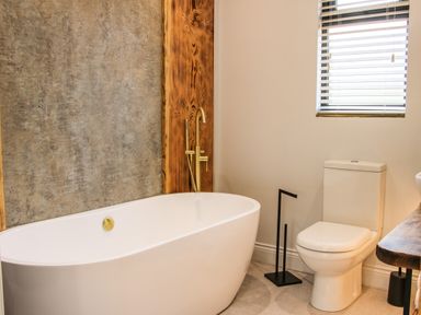 A bathroom with a freestanding bathtub a toilet a window with blinds and a wooden vanity at Meadow View in Meifod Powys