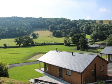 A wooden house with a slate roof on a green lawn with hills and trees in the background at Meadow View in Meifod Powys