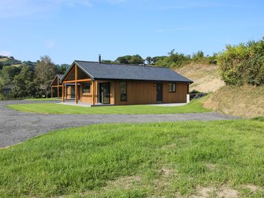 A wooden house with a front porch surrounded by grass and a gravel driveway at Meadow View in Meifod Powys