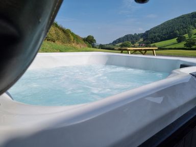An outdoor hot tub with bubbling water and a picnic table with hills and trees in the background at Meadow View in Meifod Powys