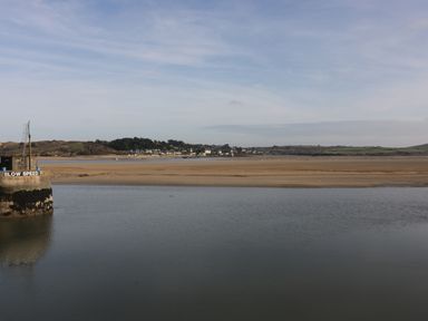 A body of water with a sandbank and buildings in the distance under a cloudy sky at Chiffchaff in Padstow
