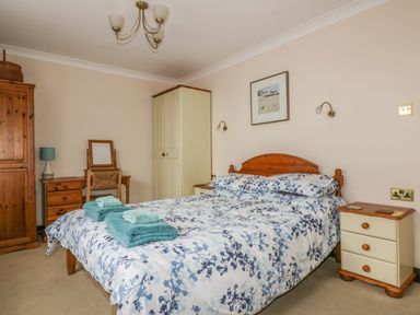 A bedroom with a bed with floral bedding and folded towels on it alongside wooden furniture at Chiffchaff in Padstow