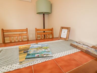 A dining table with magazines and a framed note on a polka dot table runner and wooden chairs with a floor lamp behind at Chiffchaff in Padstow