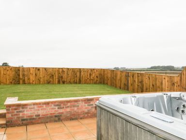 An outdoor space with a hot tub on a paved patio and a grass lawn with wooden fencing at Owl View in Lebberston near Cayton