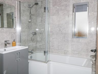 A bathroom with a bathtub and shower combination a sink with cabinet and a small window at Owl View in Lebberston near Cayton