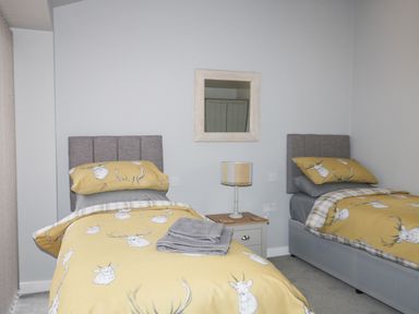 A bedroom with two single beds with yellow deer patterned bedding a bedside table with a lamp and a wall mirror at Owl View in Lebberston near Cayton