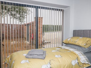 A bedroom with a bed with yellow bedding and gray towels on it near large windows with vertical blinds at Owl View in Lebberston near Cayton