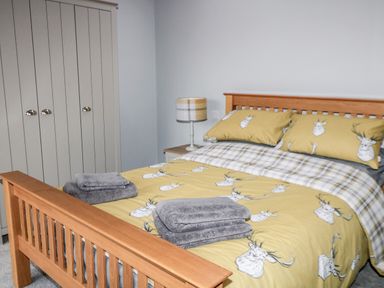 A bedroom with a wooden bed frame with yellow bedding with deer patterns and grey folded towels on the bed at Owl View in Lebberston near Cayton