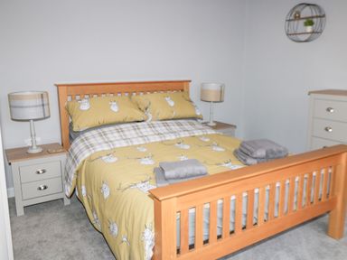 A bedroom with a wooden bed frame yellow bedding with deer patterns two bedside tables with lamps and folded towels at Owl View in Lebberston near Cayton