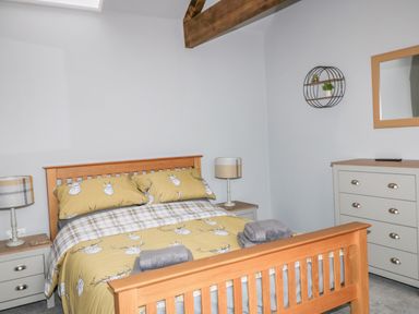 A bedroom with a wooden bed with deer patterned bedding two bedside tables with lamps a chest of drawers and a wall mirror at Owl View in Lebberston near Cayton