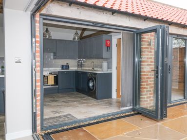 A kitchen with dark cabinets, a washing machine, oven, toaster, and open folding glass doors at Owl View in Lebberston near Cayton