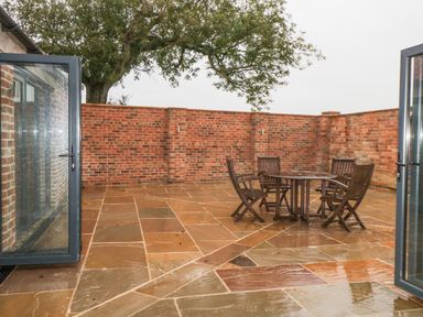 An outdoor patio area with stone flooring a round wooden table and four wooden chairs surrounded by brick walls at Owl View in Lebberston near Cayton