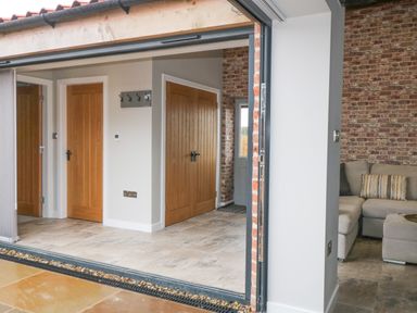 An open doorway showing an interior space with wooden doors tile flooring a coat rack and a gray sofa against a brick wall at Owl View in Lebberston near Cayton