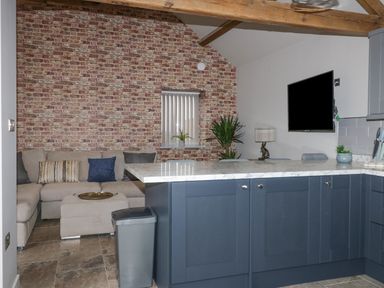 An open plan kitchen and living area with a sofa and ottoman against a brick wall at Owl View in Lebberston near Cayton