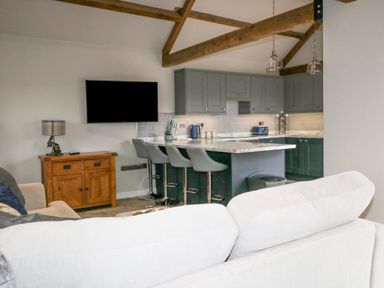 An open plan kitchen and living area with a wall mounted TV wooden cabinet and kitchen island with stools at Owl View in Lebberston near Cayton