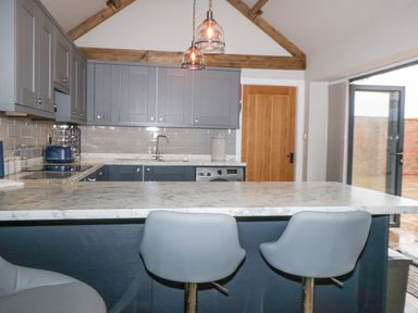 A kitchen with grey cabinets a marble countertop two stools and wooden beams at Owl View in Lebberston near Cayton