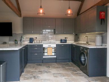 A kitchen with dark cabinets a white oven a washing machine a blue kettle and toaster on the counter at Owl View in Lebberston near Cayton