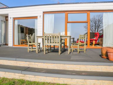 An outdoor patio with wooden table and four chairs in front of a building with large windows and sliding doors Harbour View Mudeford Christchurch