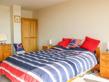 A bedroom with a double bed with striped bedding red pillows wooden wardrobes and bedside tables at Harbour View Mudeford Christchurch
