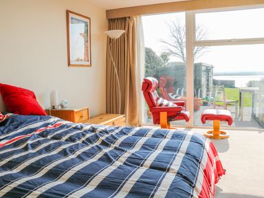 A bedroom with a striped bedspread red chair and ottoman glass door overlooking garden at Harbour View Mudeford Christchurch