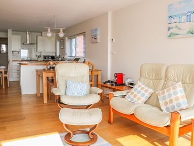 A living room with cream leather armchairs and wooden dining table at Harbour View Mudeford in Christchurch