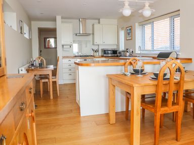A kitchen and dining area with wooden tables and chairs and white cabinets at Harbour View Mudeford in Christchurch