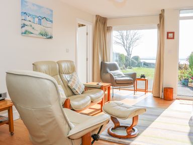 A living room with leather chairs and a footstool facing a large window and door to a garden at Harbour View Mudeford in Christchurch