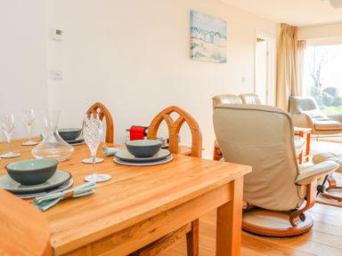 A dining table set with bowls plates glasses and napkins next to leather armchairs in a living room at Harbour View Mudeford in Christchurch