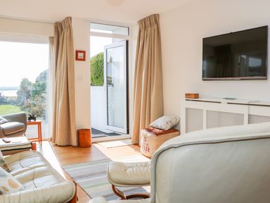 A living room with leather chairs a wall mounted television and a door opening to an outside area at Harbour View Mudeford in Christchurch