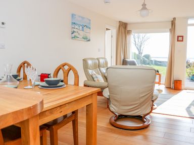 A dining table with plates and glasses beside leather chairs and a large window overlooking a garden at Harbour View Mudeford in Christchurch