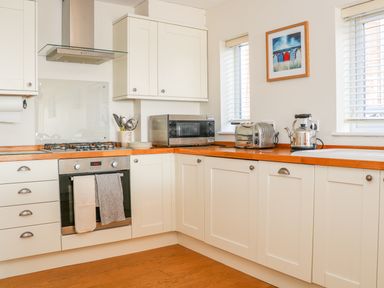 A kitchen with white cabinets wooden countertops a stove microwave toaster kettle and two windows with blinds at Harbour View Mudeford in Christchurch