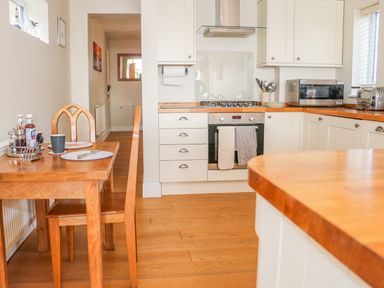 A kitchen with wooden table and chairs oven and microwave on wooden countertops at Harbour View Mudeford in Christchurch