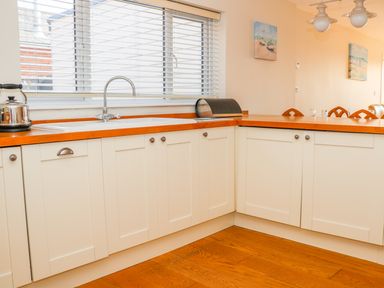 A kitchen with white cabinets wooden countertops a sink a kettle and a bread box at Harbour View Mudeford in Christchurch
