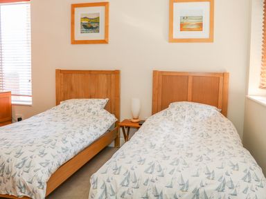 A bedroom with two single beds with wooden headboards and sailboat-patterned bedcovers in Harbour View Mudeford Christchurch