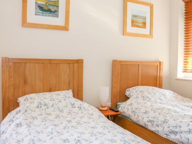 A bedroom with two single wooden beds a small wooden bedside table a lamp and remote control and two framed pictures on the wall at Harbour View Mudeford in Christchurch