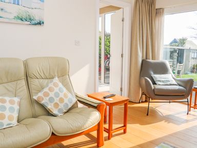 A living room with two armchairs a wooden side table and a large window showing a garden at Harbour View Mudeford Christchurch