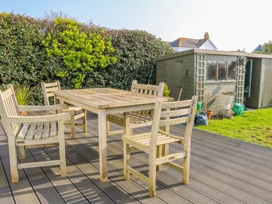 A wooden outdoor table with four chairs on a deck next to a garden shed and hedge at Harbour View Mudeford in Christchurch
