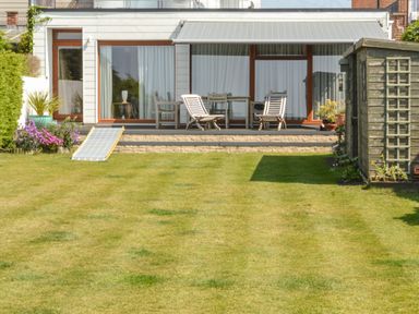 A backyard with wooden deck chairs a table a shed plants and a lawn at Harbour View Mudeford Christchurch